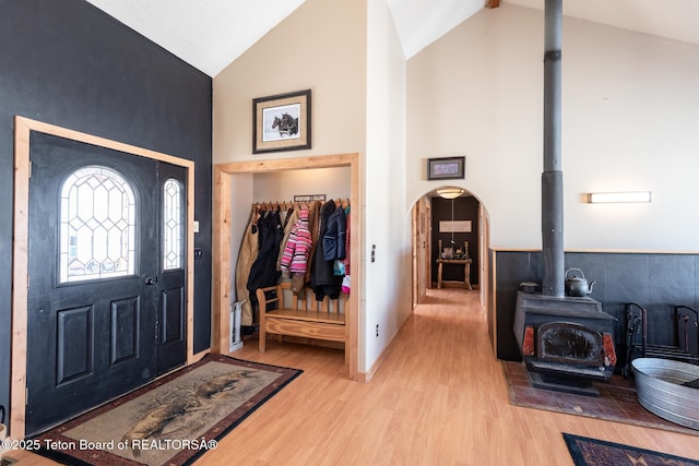 foyer with a wood stove, high vaulted ceiling, arched walkways, and wood finished floors