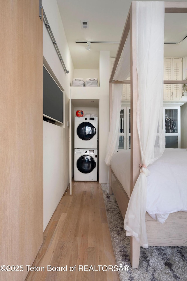 laundry room featuring stacked washing maching and dryer, track lighting, laundry area, and wood finished floors