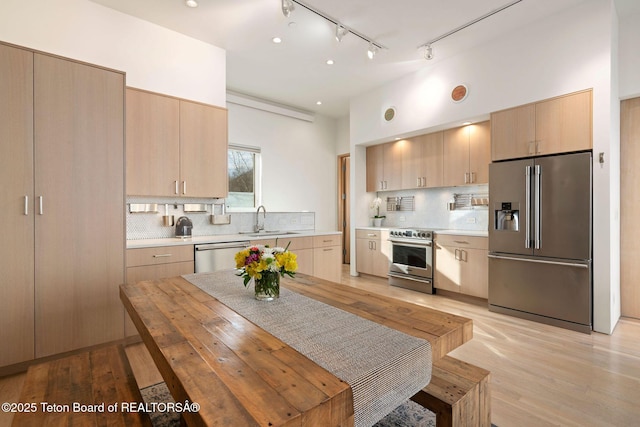 kitchen featuring decorative backsplash, premium appliances, light countertops, light brown cabinets, and a sink