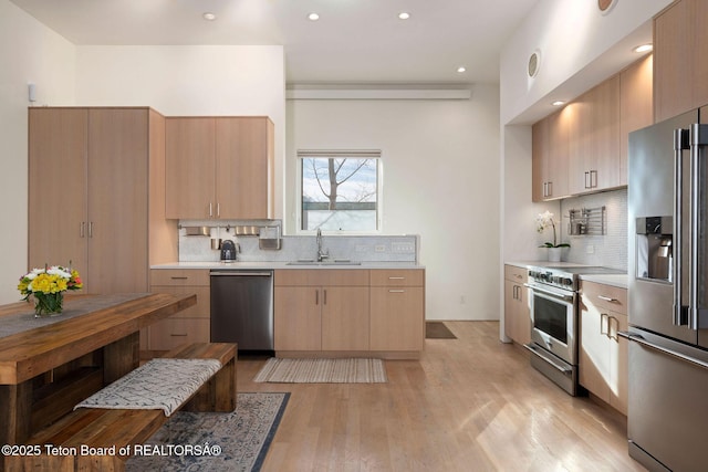 kitchen featuring decorative backsplash, high end appliances, light countertops, light wood-style floors, and a sink