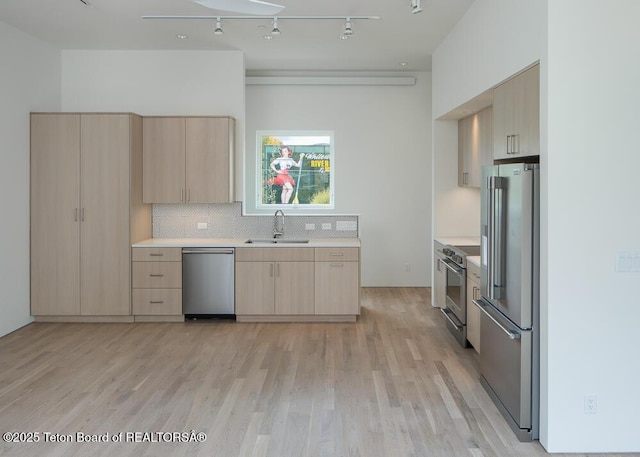 kitchen with high end appliances, tasteful backsplash, light countertops, light brown cabinetry, and a sink