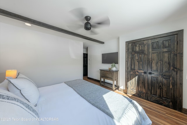 bedroom with ceiling fan, a closet, wood finished floors, and beamed ceiling