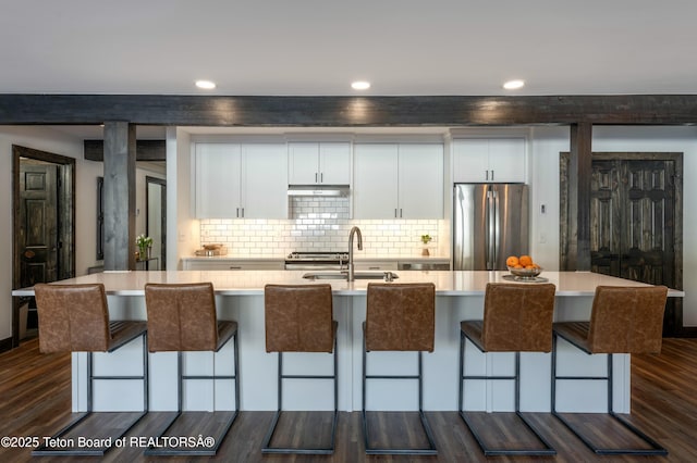 kitchen featuring dark wood-style flooring, a sink, freestanding refrigerator, and white cabinetry