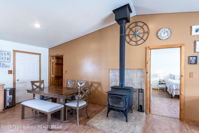 dining area with a wood stove, light wood finished floors, and lofted ceiling