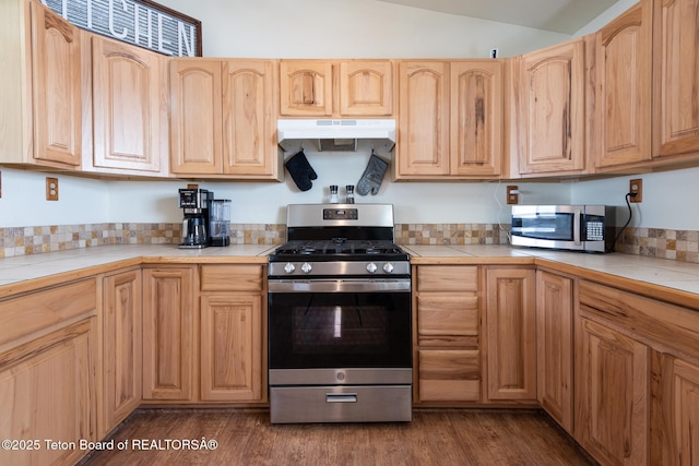 kitchen featuring under cabinet range hood, light brown cabinets, dark wood-style floors, and appliances with stainless steel finishes