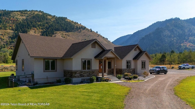 view of front of property with a front yard, stucco siding, stone siding, dirt driveway, and a mountain view