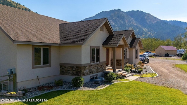 view of side of home with stone siding, a mountain view, roof with shingles, and dirt driveway