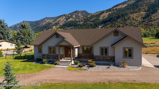 view of front of house with stone siding, a mountain view, a front yard, and fence