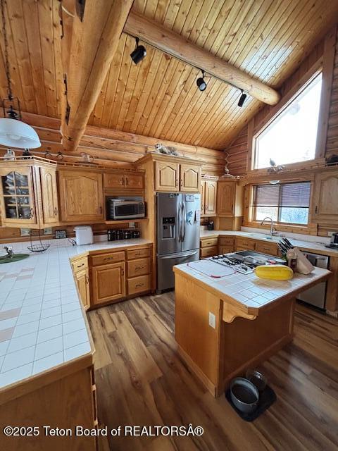 kitchen featuring tile counters, wooden ceiling, appliances with stainless steel finishes, vaulted ceiling with beams, and track lighting