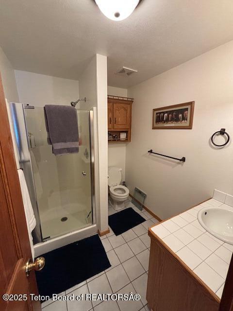 bathroom featuring toilet, vanity, visible vents, a shower stall, and tile patterned floors