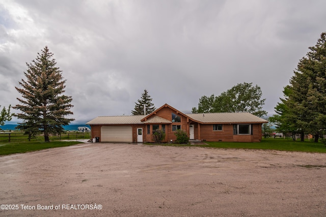 view of front facade with an attached garage, fence, driveway, and metal roof