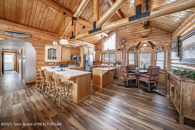 kitchen featuring arched walkways, beam ceiling, appliances with stainless steel finishes, and a center island