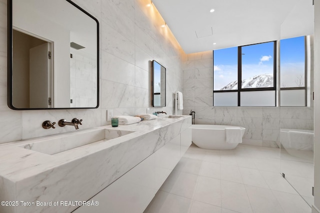 bathroom featuring tile patterned flooring, double vanity, a freestanding tub, tile walls, and a sink