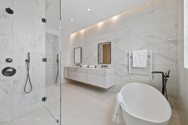 full bath featuring radiator, a marble finish shower, a soaking tub, double vanity, and tile walls