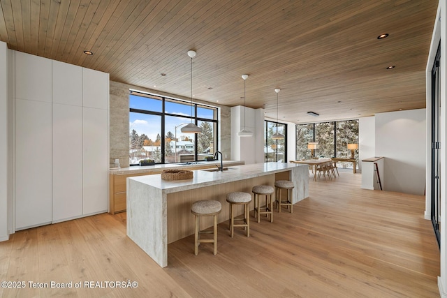 kitchen with light wood-style flooring, wood ceiling, a kitchen bar, and expansive windows