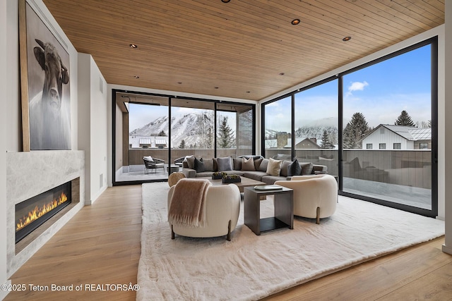 living room featuring a glass covered fireplace, wooden ceiling, floor to ceiling windows, and wood finished floors