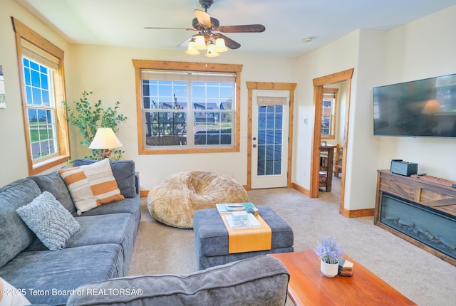 living area with ceiling fan, baseboards, carpet flooring, and a glass covered fireplace