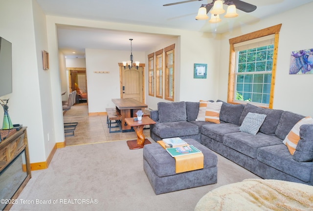 living area featuring ceiling fan with notable chandelier, carpet flooring, and baseboards