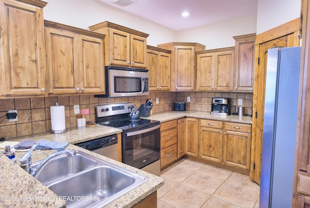 kitchen with light tile patterned flooring, a sink, appliances with stainless steel finishes, tasteful backsplash, and brown cabinetry