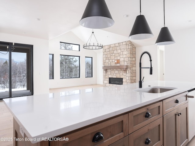 kitchen with lofted ceiling, hanging light fixtures, light countertops, a stone fireplace, and a sink