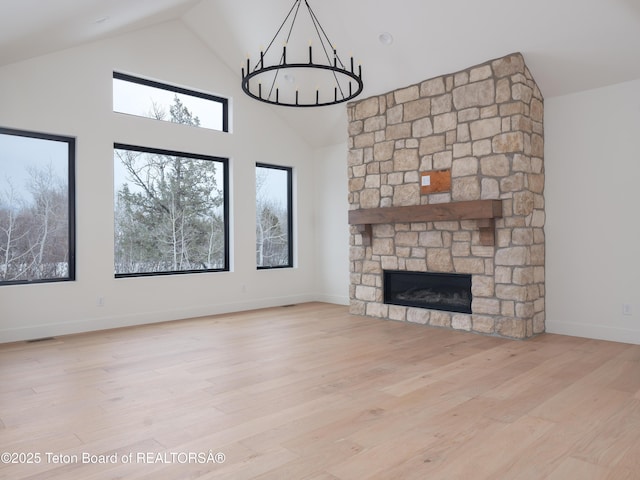 unfurnished living room with a notable chandelier, a fireplace, wood finished floors, high vaulted ceiling, and baseboards