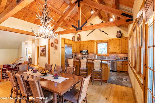 dining area with light wood finished floors, wooden ceiling, an inviting chandelier, high vaulted ceiling, and beam ceiling