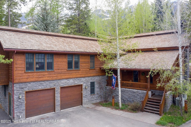 rustic home featuring aphalt driveway, roof with shingles, stairway, a garage, and stone siding