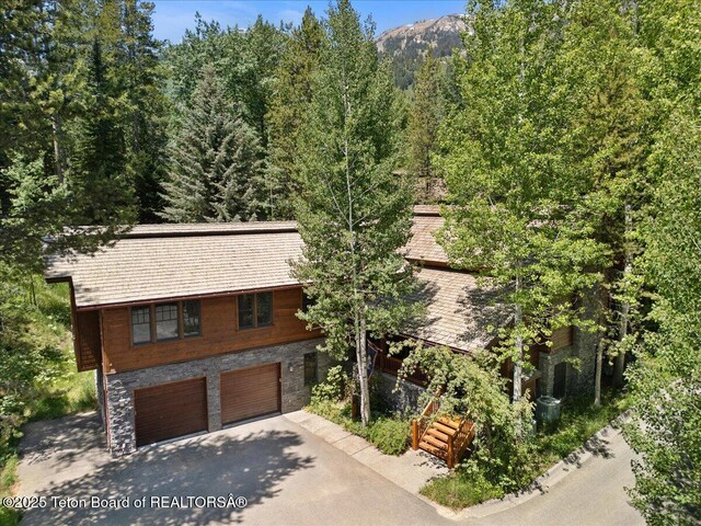 3102 W Arrowhead Rd, Teton Village, WY 83025 - view of front of home featuring asphalt driveway, an attached garage, stone siding, and a view of trees