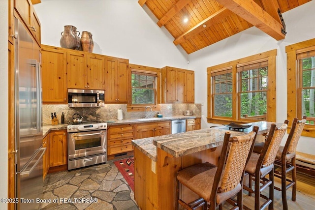 3102 W Arrowhead Rd, Teton Village, WY 83025 - kitchen with appliances with stainless steel finishes, a wooden ceiling with exposed beams, tasteful backsplash, high vaulted ceiling, and a breakfast bar area