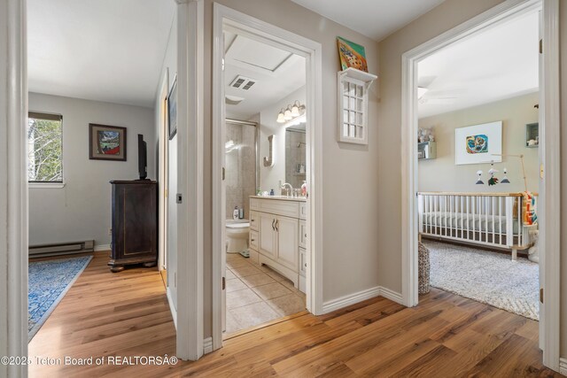 corridor with a baseboard heating unit, attic access, visible vents, and light wood-type flooring