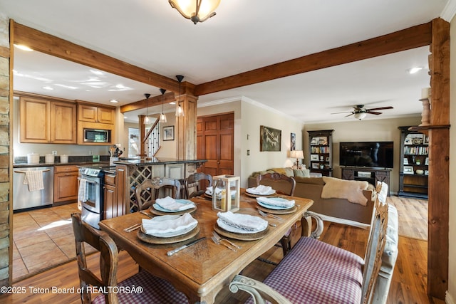 dining space with beam ceiling, light wood finished floors, stairs, and a ceiling fan