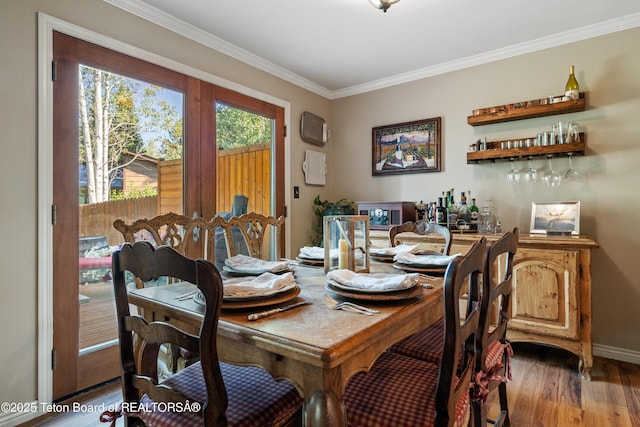 dining space featuring a bar, light wood-style floors, baseboards, and ornamental molding