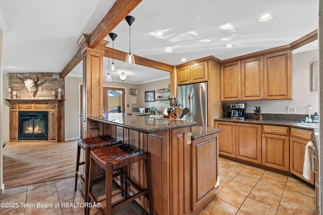 kitchen featuring beam ceiling, ornamental molding, stainless steel refrigerator, a kitchen breakfast bar, and brown cabinetry