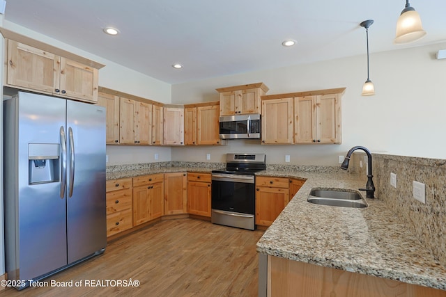 kitchen with light stone countertops, light brown cabinets, stainless steel appliances, and a sink