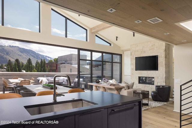 kitchen with light wood-style flooring, a fireplace, a sink, beamed ceiling, and a mountain view