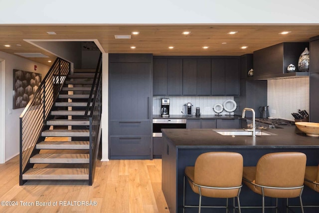 kitchen with a sink, a breakfast bar area, dark countertops, and wall chimney exhaust hood