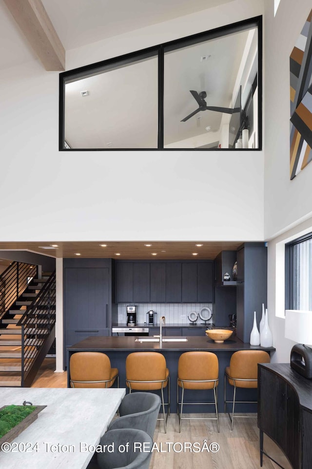 dining area featuring stairway, light wood-style flooring, a high ceiling, and ceiling fan