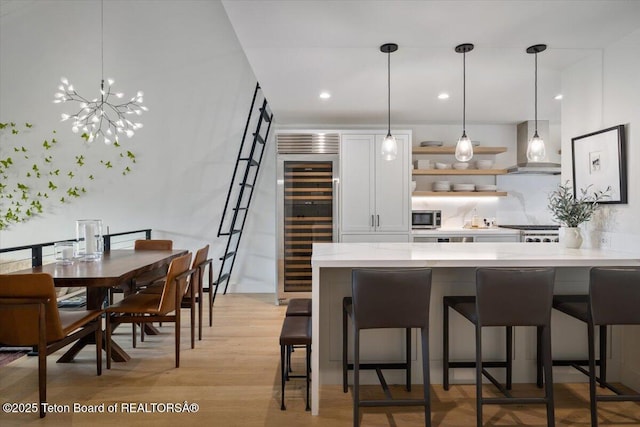 kitchen with stainless steel microwave, wine cooler, a breakfast bar, and wall chimney range hood