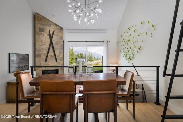 dining area featuring a notable chandelier, wood finished floors, a stone fireplace, wood ceiling, and vaulted ceiling