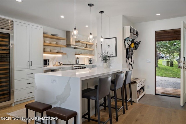 kitchen featuring open shelves, a kitchen breakfast bar, white cabinets, wall chimney range hood, and range