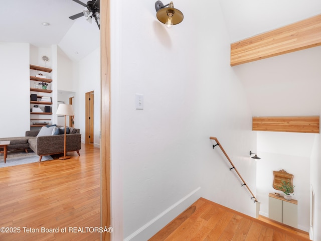 staircase with ceiling fan, baseboards, beamed ceiling, wood finished floors, and high vaulted ceiling