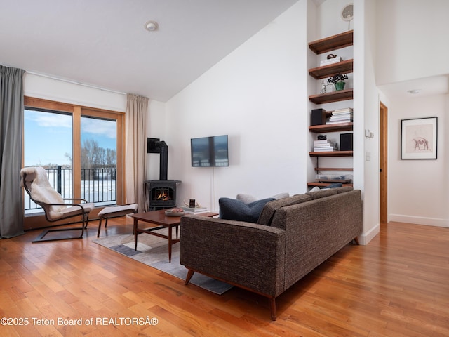 living room with light wood finished floors, high vaulted ceiling, a wood stove, and baseboards