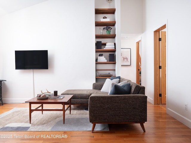 living area with built in shelves, wood finished floors, and baseboards