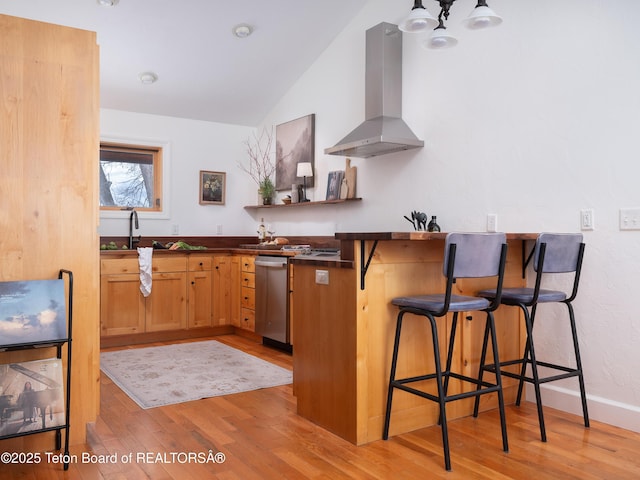 kitchen featuring light wood finished floors, a breakfast bar, dishwasher, dark countertops, and exhaust hood