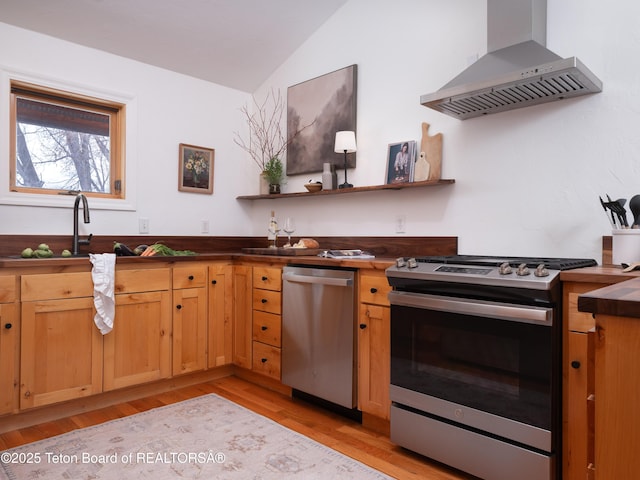 kitchen with light wood-type flooring, lofted ceiling, stainless steel appliances, wall chimney exhaust hood, and a sink