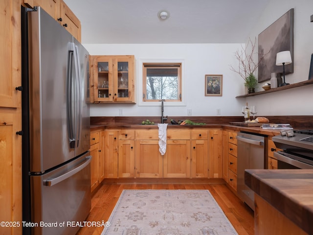 kitchen with light wood-type flooring, glass insert cabinets, dark countertops, and appliances with stainless steel finishes