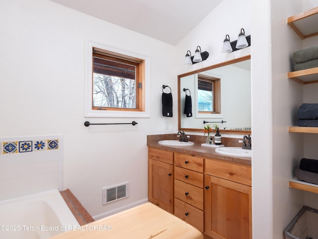 bathroom featuring double vanity, a tub to relax in, visible vents, and a sink