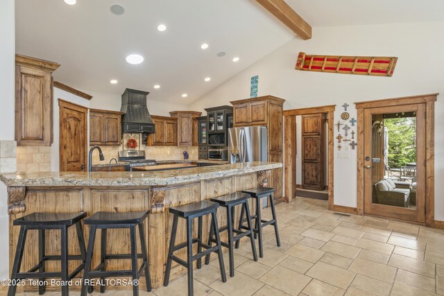 2035 Tomahawk Trl, Victor, ID 83455 - kitchen with decorative backsplash, a peninsula, light stone counters, custom range hood, and appliances with stainless steel finishes