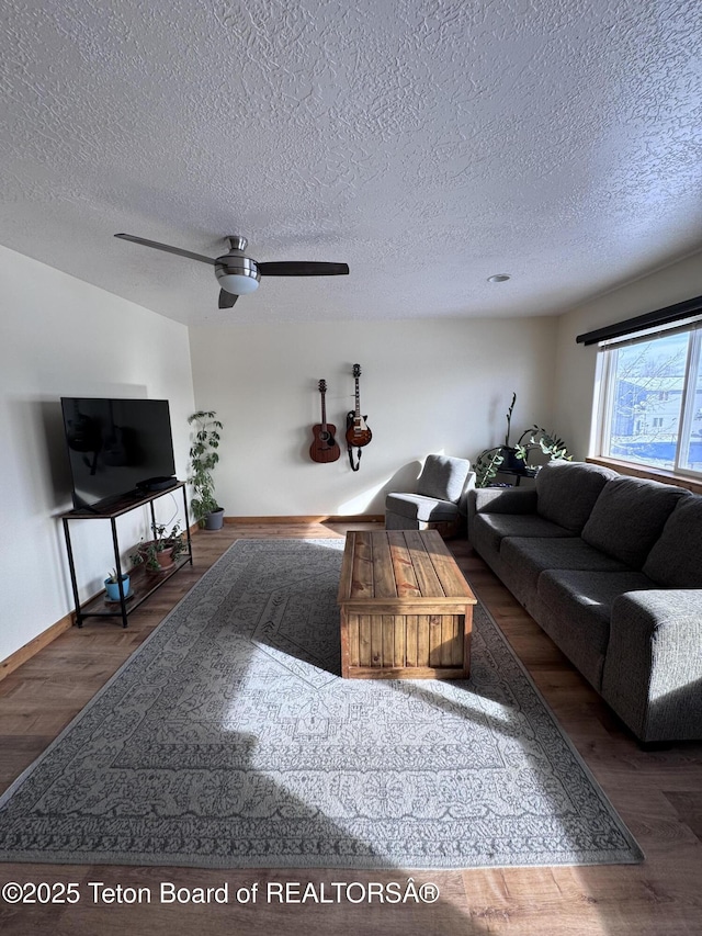 living room with a ceiling fan, wood finished floors, baseboards, and a textured ceiling