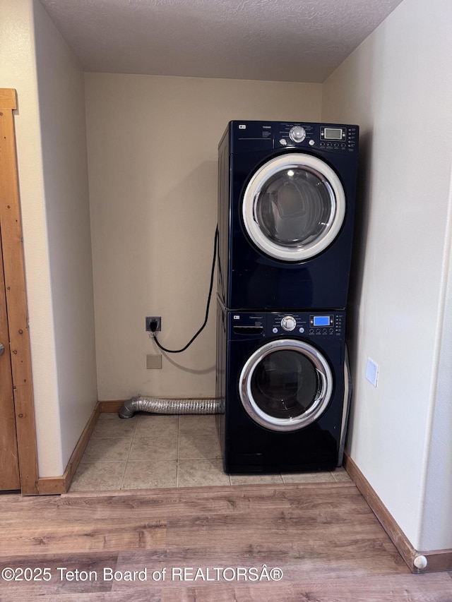 clothes washing area with baseboards, wood finished floors, laundry area, and stacked washing maching and dryer